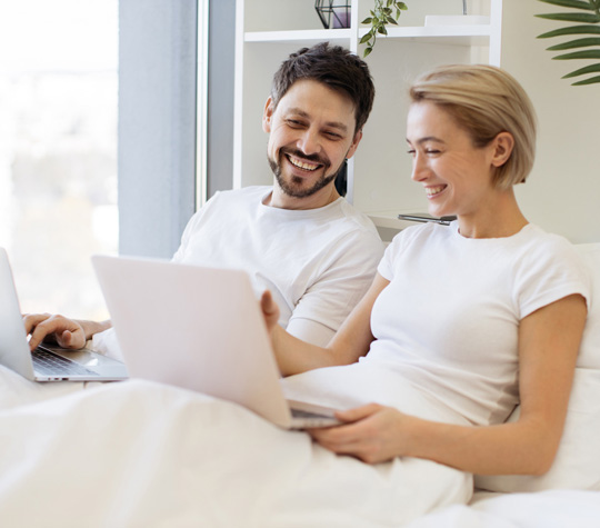Young couple sitting on a bed with laptops